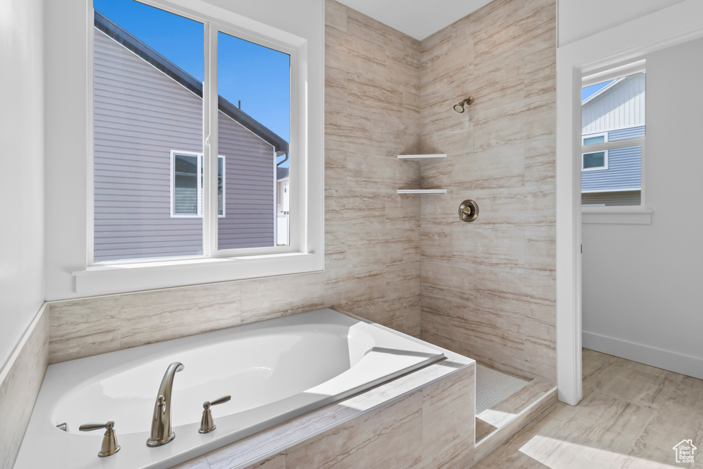 Bathroom with tiled shower, a bath, and baseboards