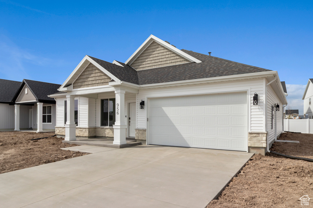 View of front of property with a porch, driveway, an attached garage, stone siding, and a shingled roof