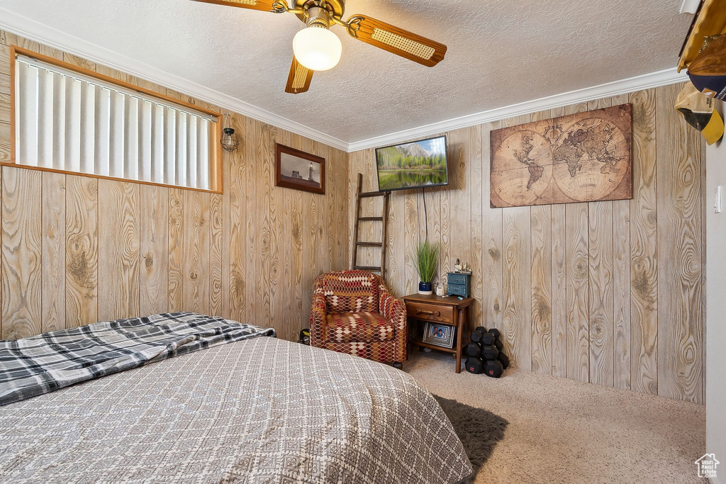 Bedroom with carpet, wood walls, a textured ceiling, crown molding, and ceiling fan