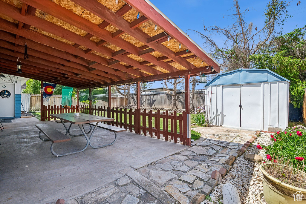 View of patio / terrace featuring a storage unit, a fenced backyard, an outdoor structure, and outdoor dining area