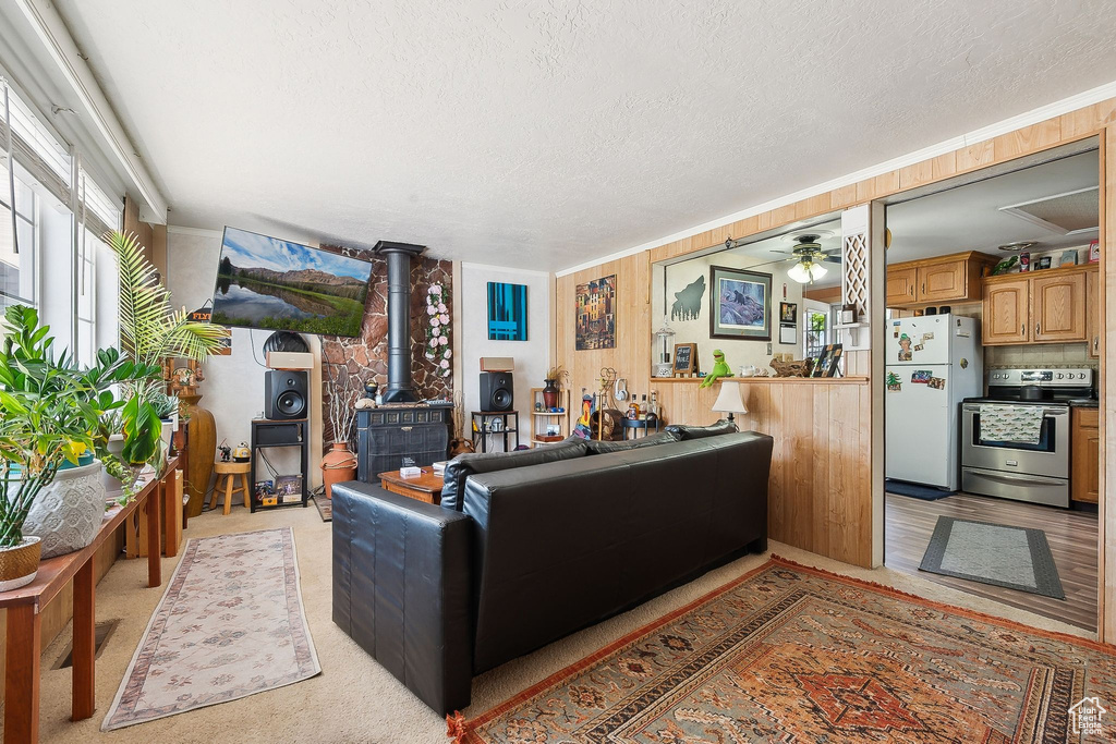 Living room with a wood stove, a textured ceiling, ceiling fan, and light colored carpet