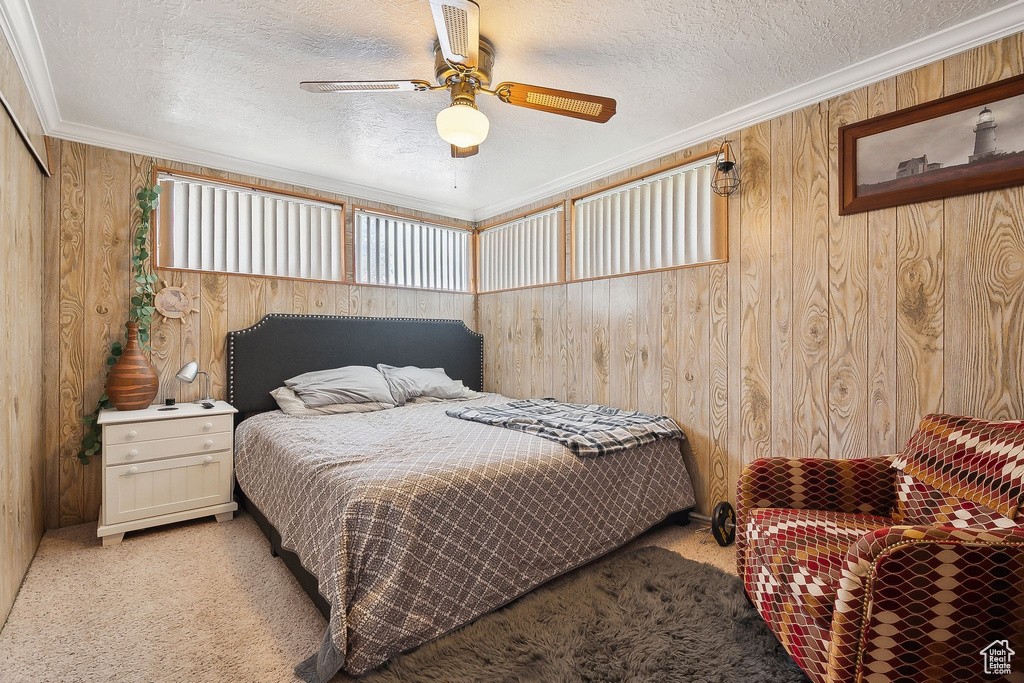Bedroom with light carpet, a textured ceiling, wooden walls, crown molding, and ceiling fan
