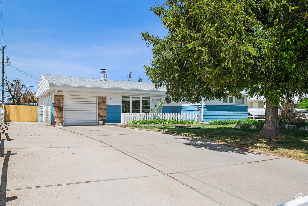 View of front of house featuring concrete driveway, an attached garage, a fenced front yard, and a shingled roof