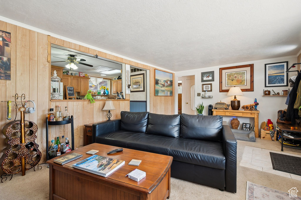 Living area with light carpet, a ceiling fan, wooden walls, and a textured ceiling