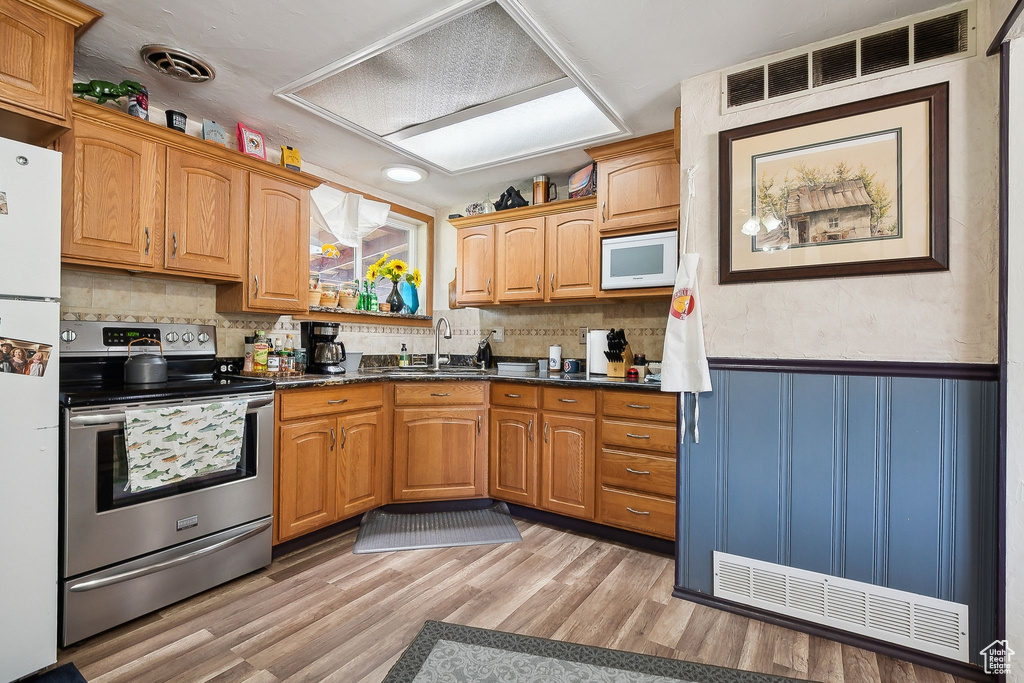 Kitchen featuring white appliances, a sink, wainscoting, dark countertops, and light wood-style floors