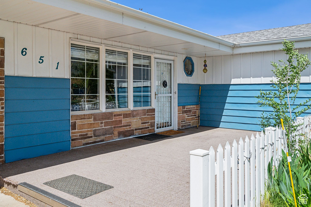 View of exterior entry with board and batten siding, roof with shingles, covered porch, and fence