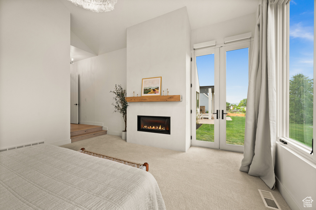 Carpeted bedroom with access to outside, a glass covered fireplace, a chandelier, and french doors