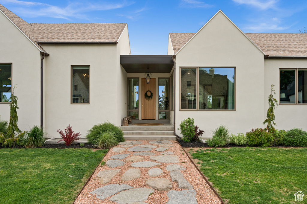 View of front facade featuring a shingled roof, stucco siding, and a front lawn