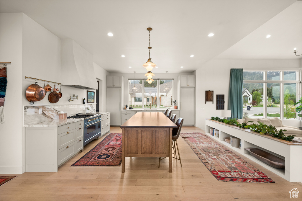 Kitchen with range with two ovens, light wood finished floors, recessed lighting, premium range hood, and hanging light fixtures