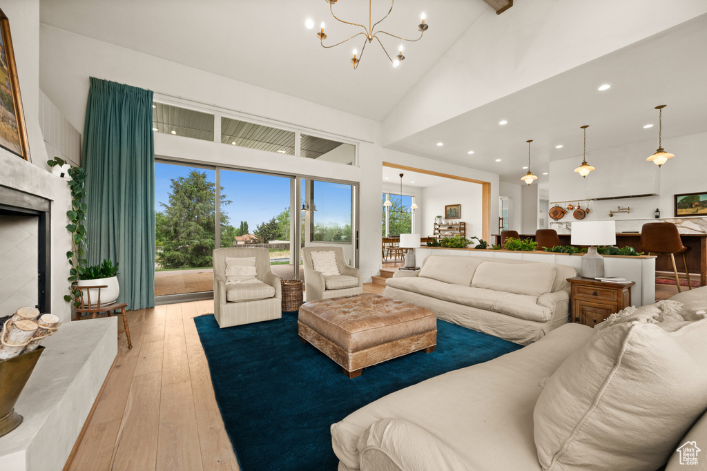 Living area with high vaulted ceiling, light wood-style flooring, a chandelier, recessed lighting, and a fireplace with raised hearth