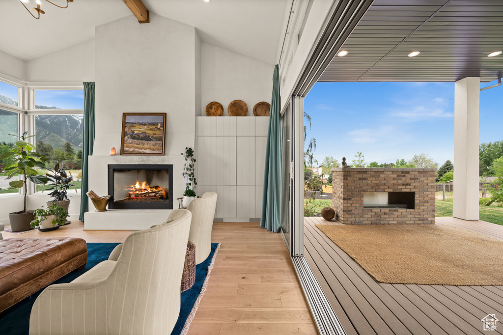 Living area with a warm lit fireplace, light wood finished floors, beamed ceiling, recessed lighting, and high vaulted ceiling