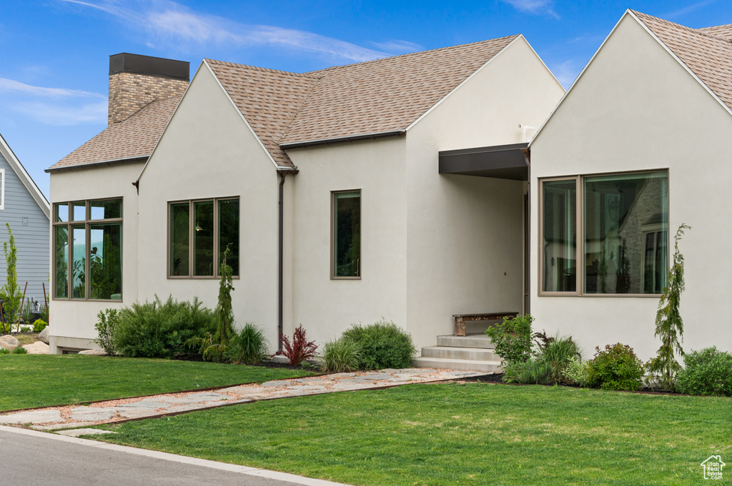 View of front facade with stucco siding, a chimney, roof with shingles, and a front yard