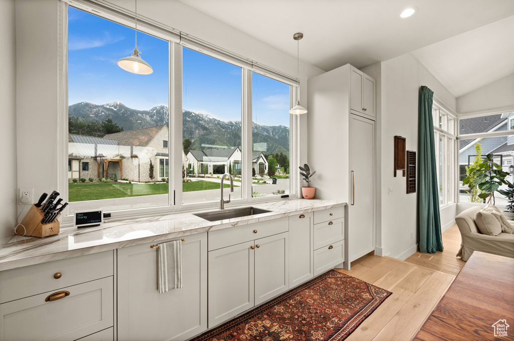 Kitchen with a sink, a mountain view, light wood-style flooring, light stone counters, and pendant lighting