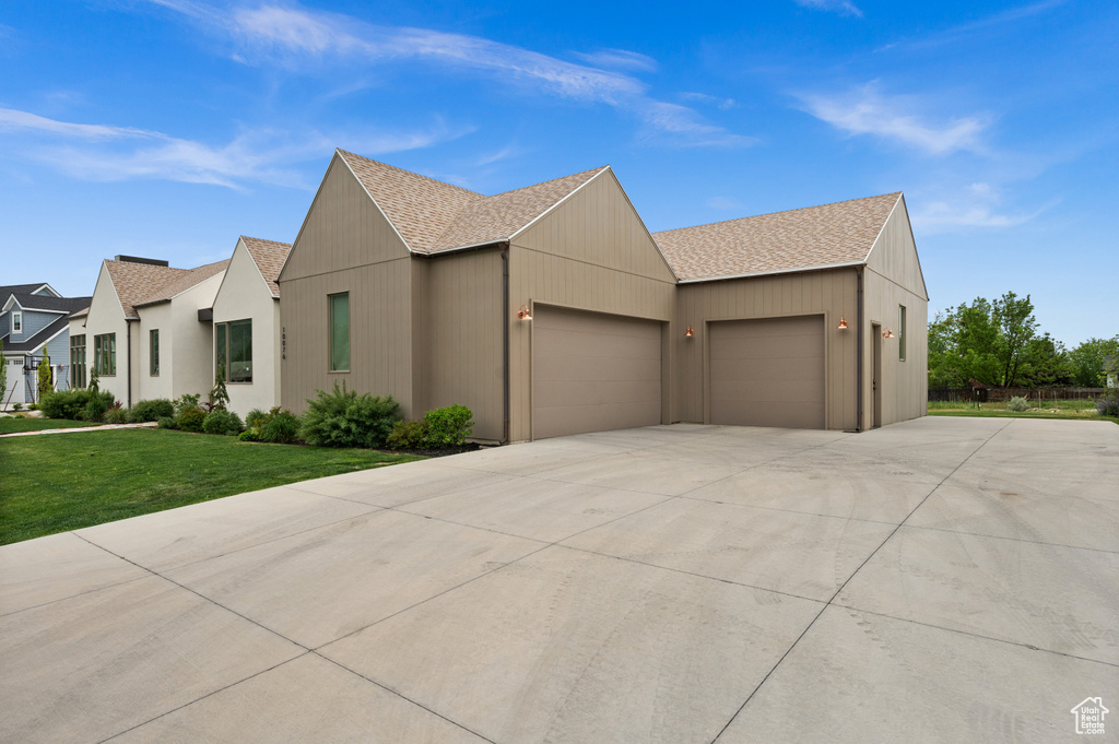 View of front of property with a garage, roof with shingles, driveway, and a front yard