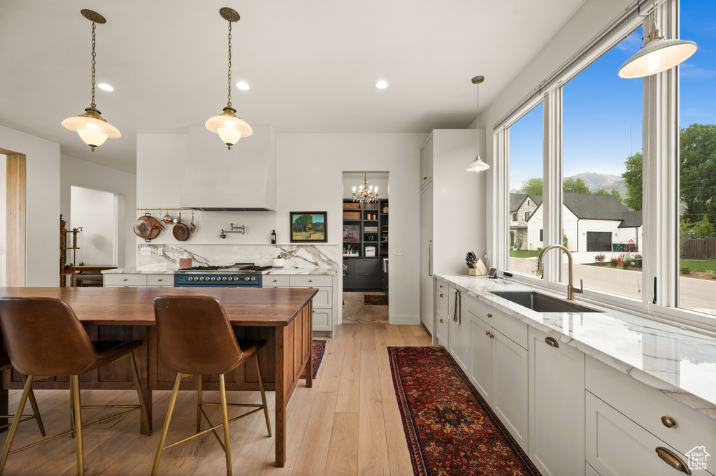 Kitchen with a sink, gas range oven, light wood-style flooring, a chandelier, and pendant lighting