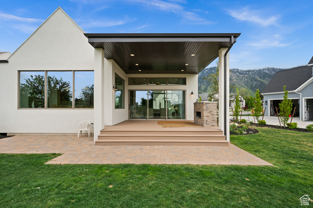 Rear view of house featuring stucco siding, a yard, a mountain view, and a patio