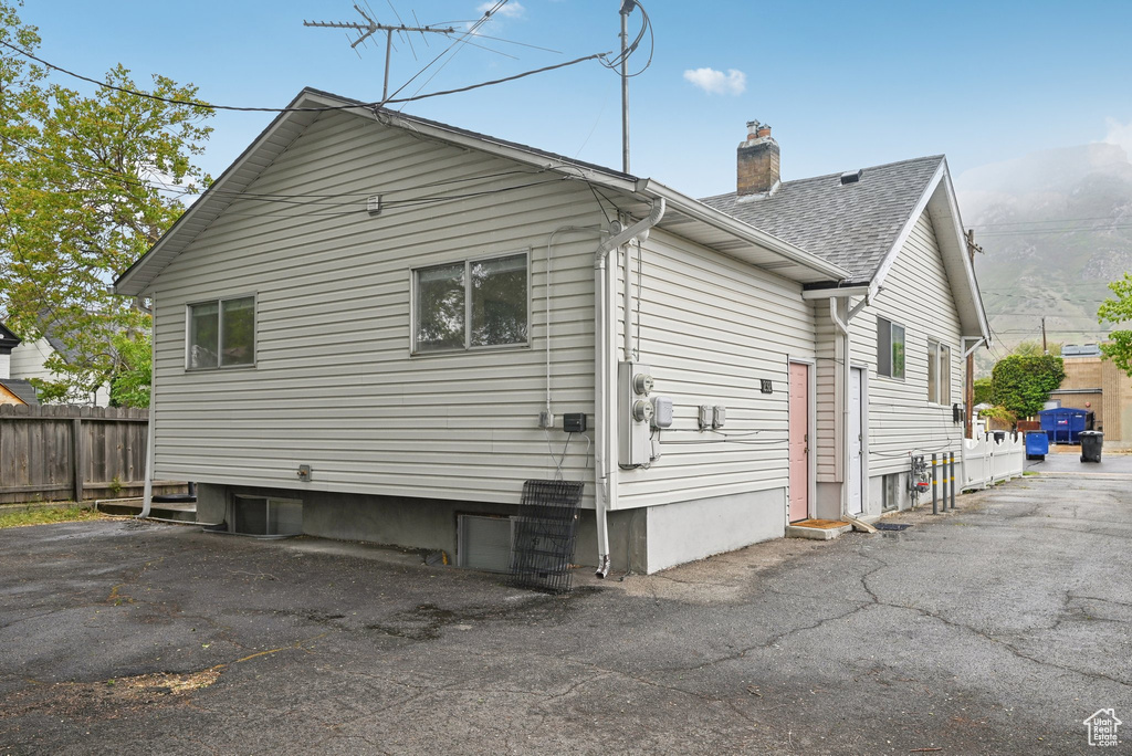 View of property exterior featuring a chimney, fence, and roof with shingles