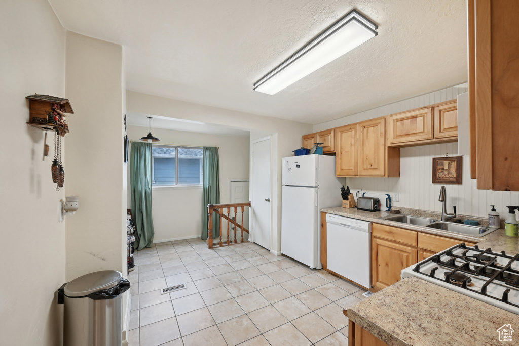 Kitchen featuring white appliances, a sink, light brown cabinets, light countertops, and light tile patterned floors