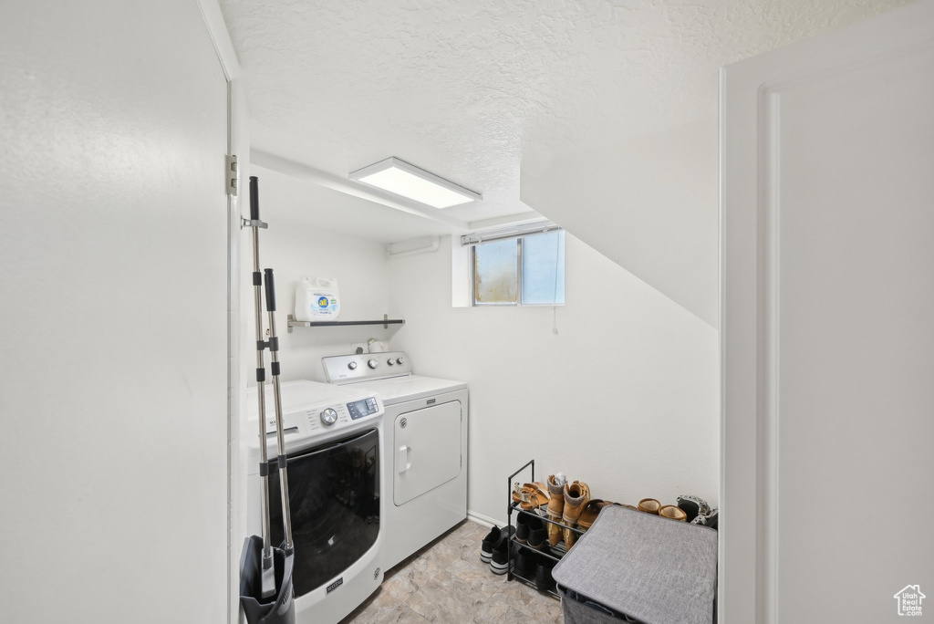 Washroom with washing machine and clothes dryer, a textured ceiling, and light stone finish flooring