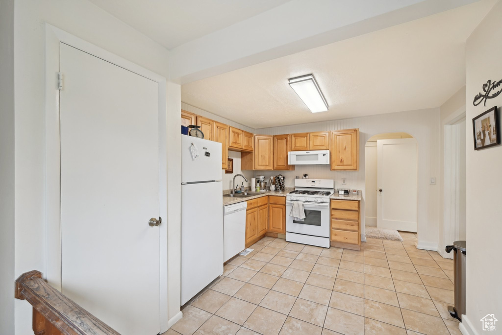 Kitchen featuring white appliances, light countertops, light brown cabinetry, light tile patterned floors, and a sink