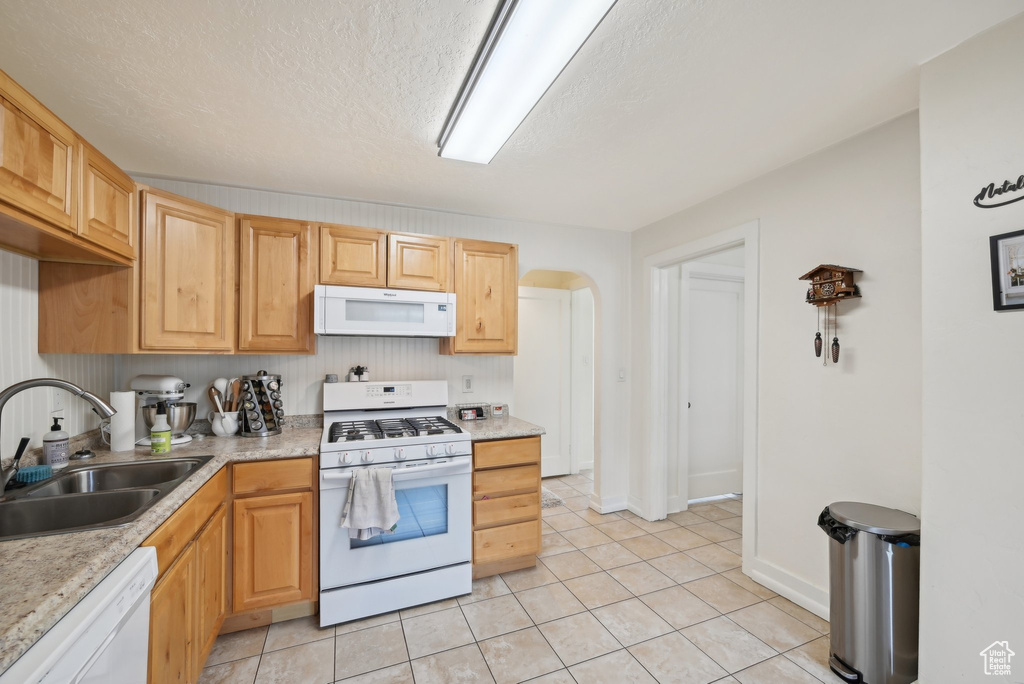 Kitchen featuring white appliances, a sink, light countertops, arched walkways, and light tile patterned floors