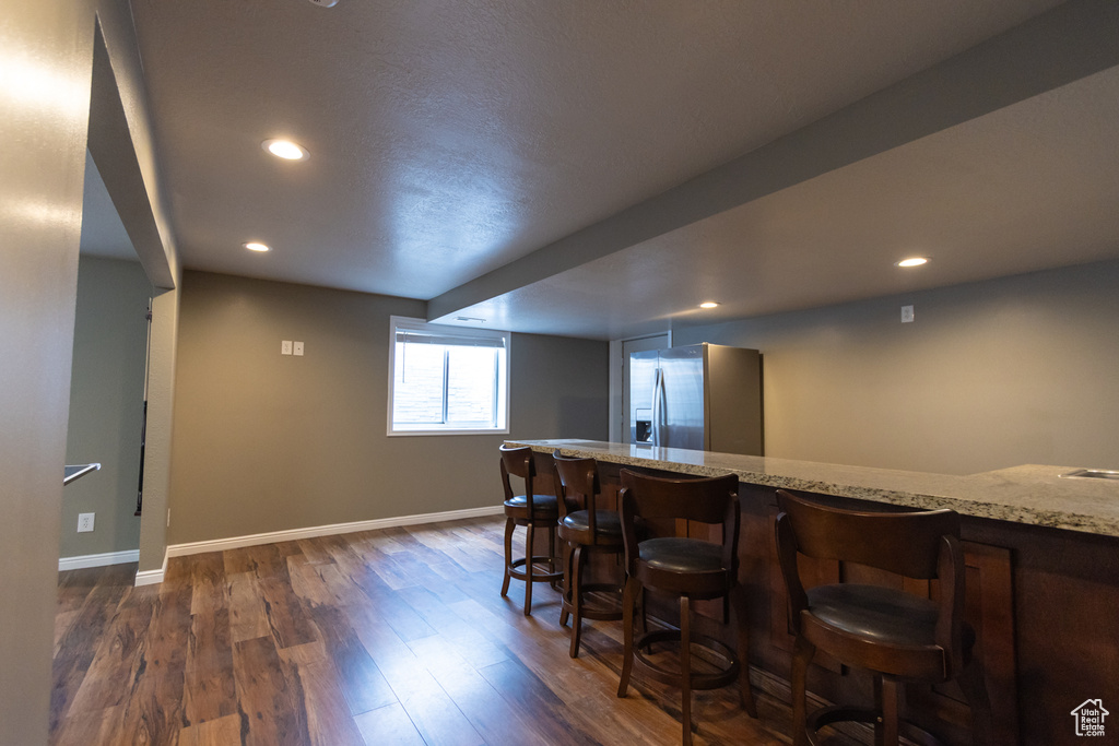 Indoor bar featuring stainless steel fridge with ice dispenser, dark wood finished floors, baseboards, and recessed lighting