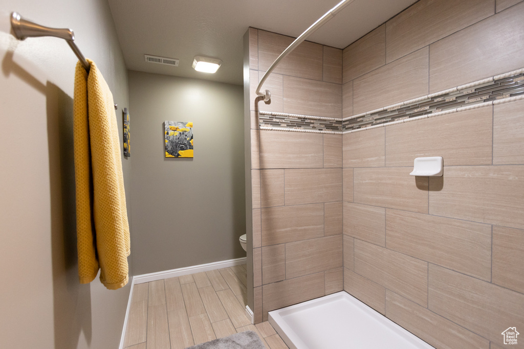Full bathroom featuring a tile shower, toilet, baseboards, and wood finish floors