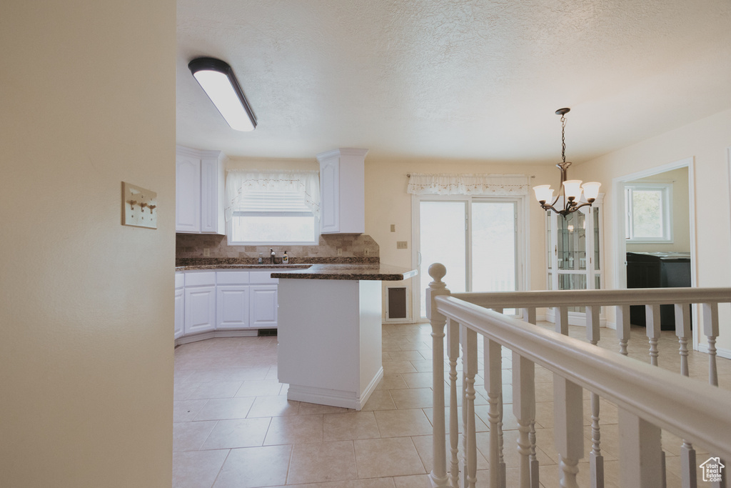 Kitchen with dark countertops, a chandelier, white cabinets, decorative backsplash, and light tile patterned floors