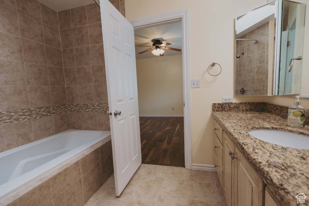Full bathroom featuring tiled tub, a tile shower, ceiling fan, vanity, and baseboards