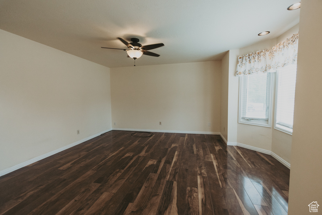 Empty room featuring dark wood-style flooring, ceiling fan, and baseboards