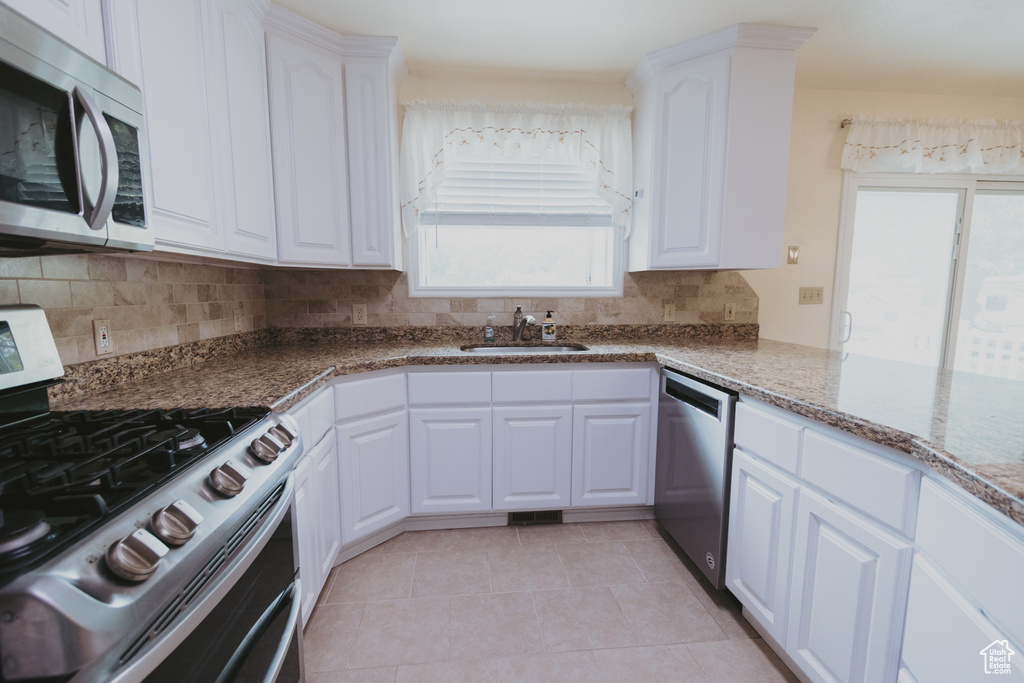 Kitchen featuring appliances with stainless steel finishes, a sink, backsplash, white cabinetry, and light tile patterned flooring