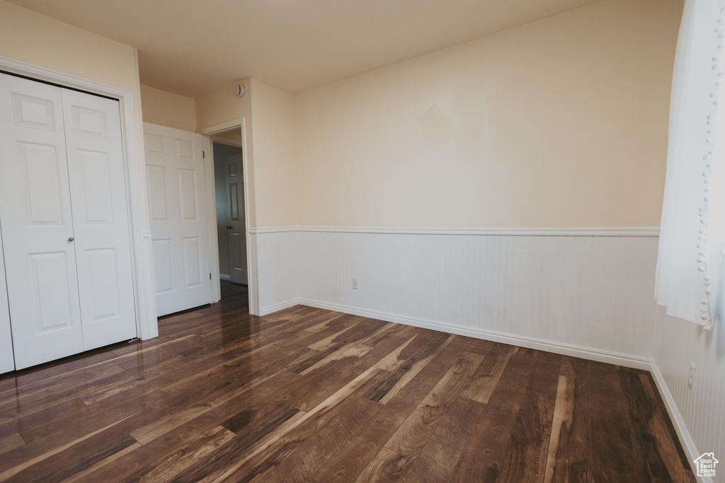 Unfurnished bedroom featuring wood finished floors, wainscoting, a closet, and baseboards