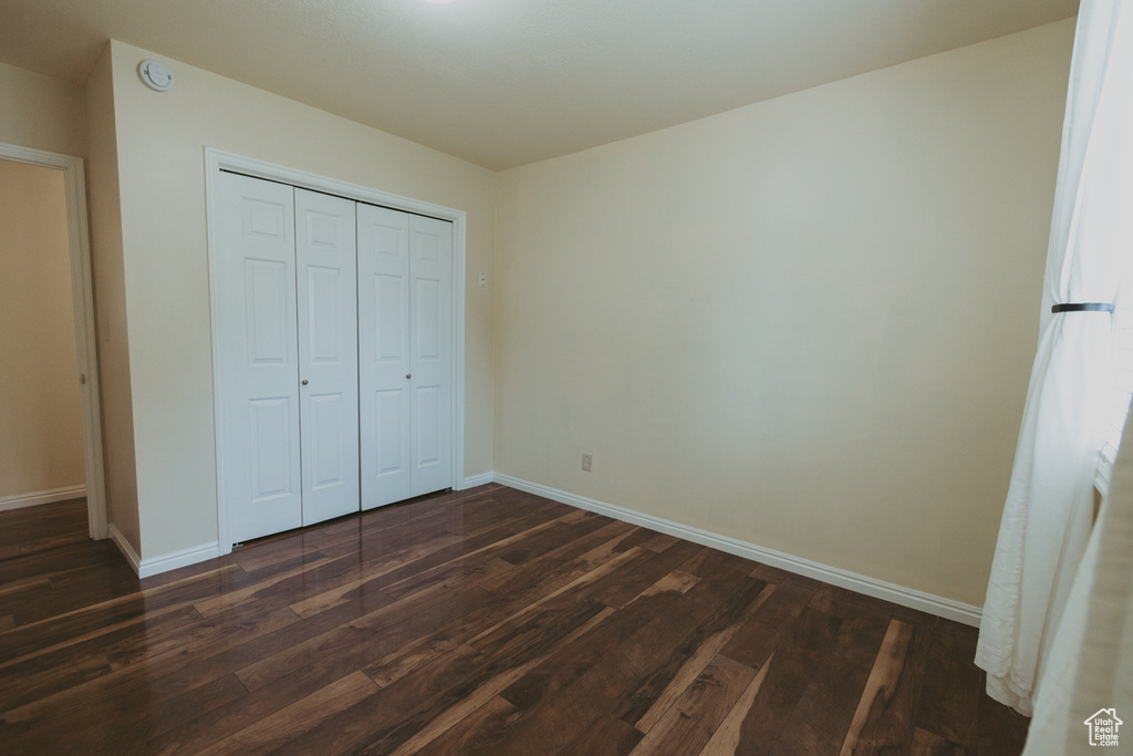 Unfurnished bedroom with dark wood-style flooring, baseboards, and a closet