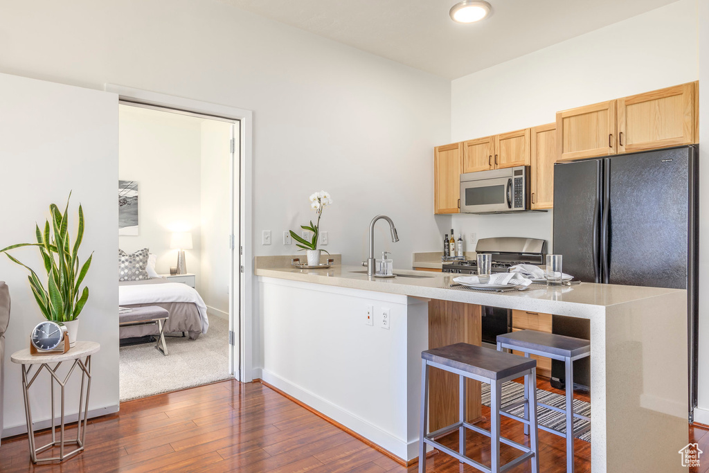 Kitchen with stainless steel appliances, a sink, light brown cabinetry, a breakfast bar area, and dark wood finished floors