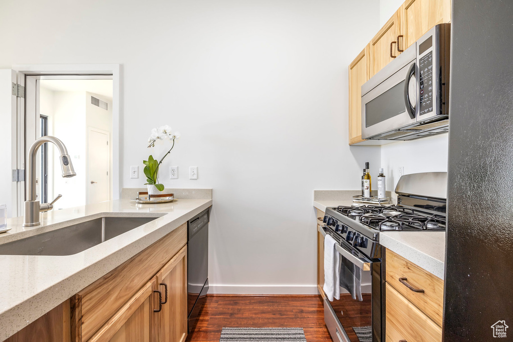 Kitchen with stainless steel appliances, a sink, dark wood-type flooring, baseboards, and light brown cabinets