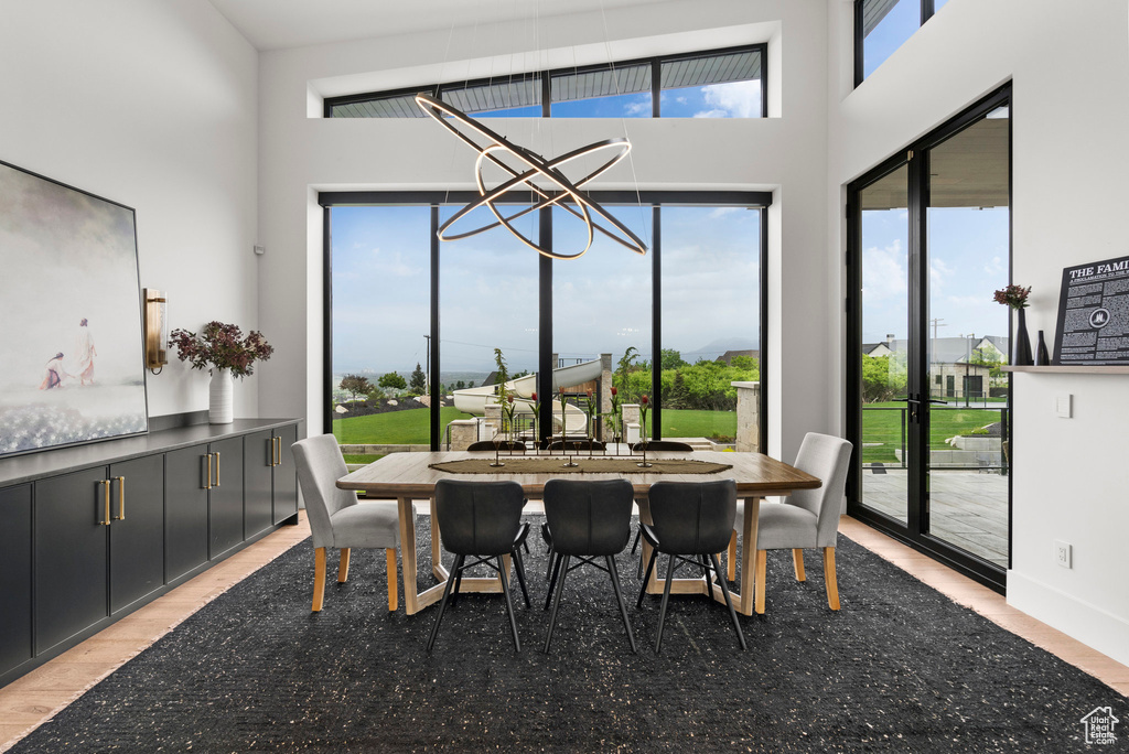 Dining room with light wood-type flooring, a towering ceiling, and a chandelier