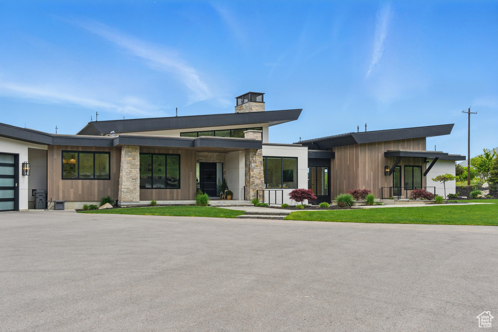 Contemporary home featuring a chimney, a garage, stone siding, and asphalt driveway