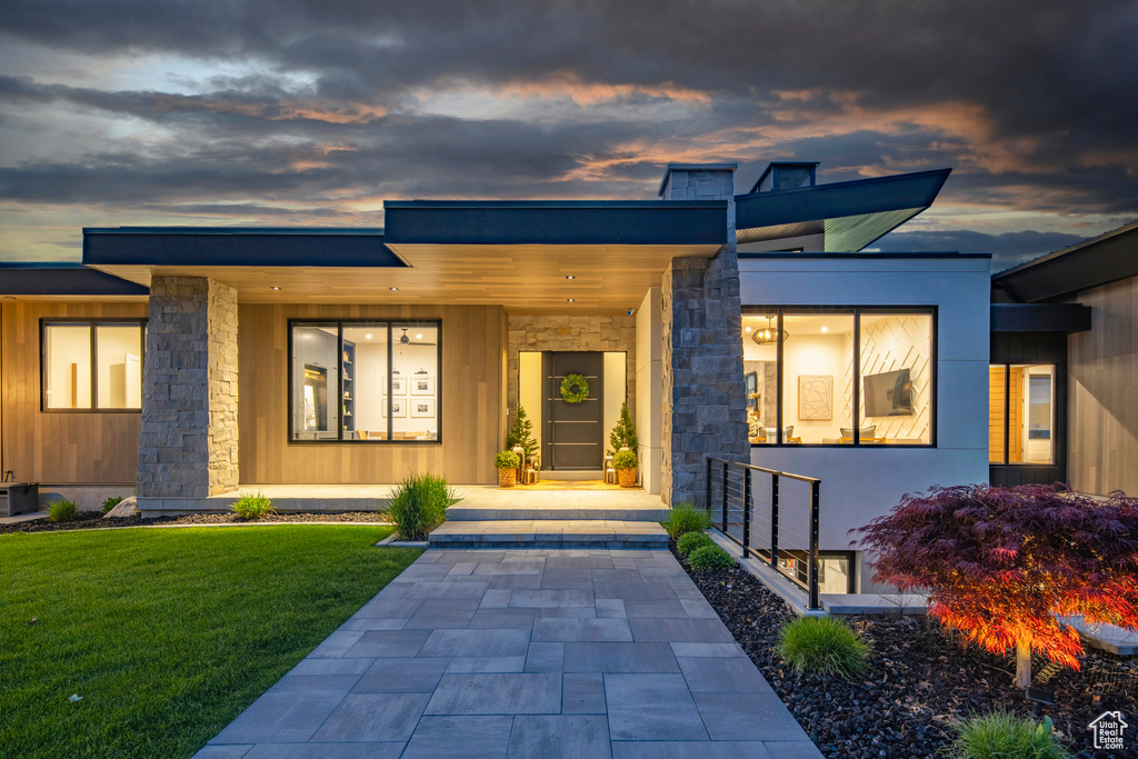 Exterior entry at dusk with stone siding and a lawn