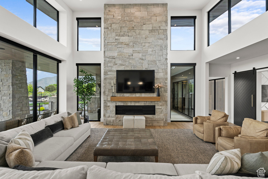 Living room with a stone fireplace, a barn door, a towering ceiling, and wood finished floors
