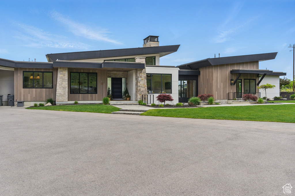 Contemporary house featuring a chimney, a front lawn, stone siding, and covered porch