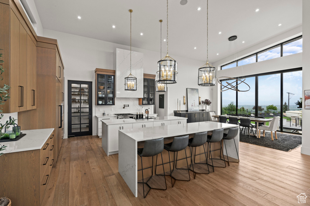 Kitchen with a spacious island, light wood finished floors, a chandelier, a kitchen bar, and glass insert cabinets