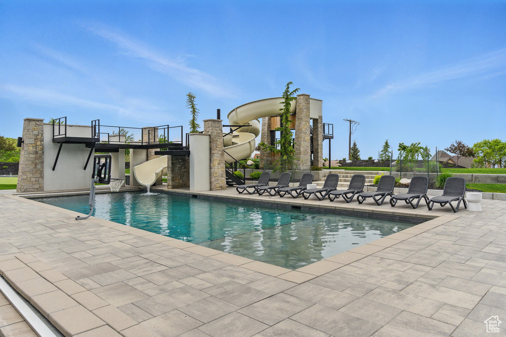 Outdoor pool featuring a water slide and a patio