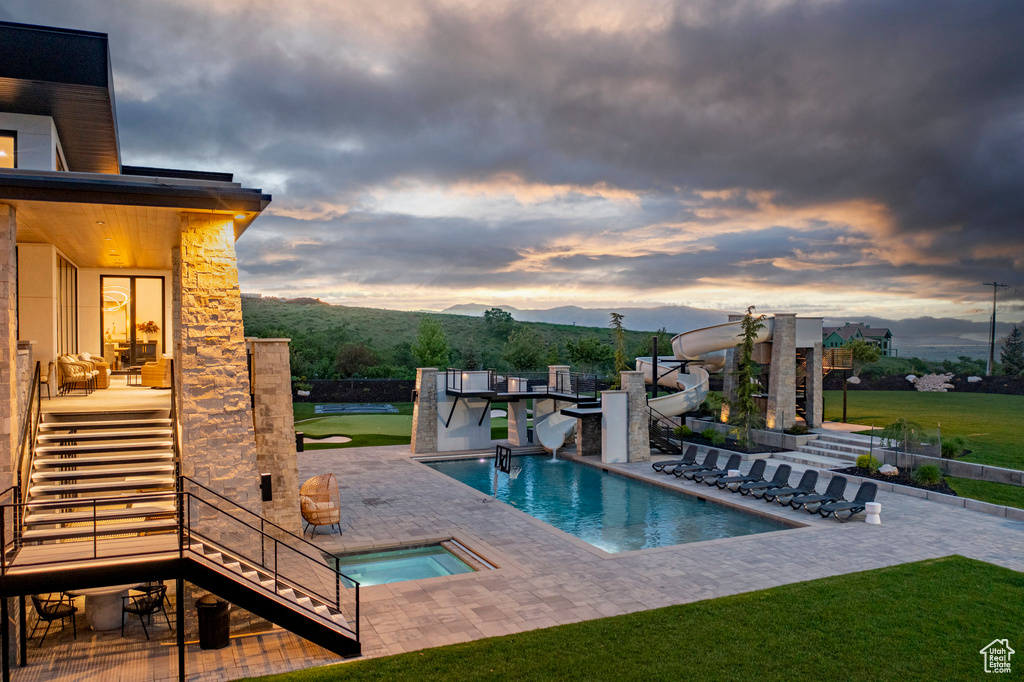 Pool at dusk featuring a water slide, an in-ground hot tub, stairway, a patio, and a mountain view