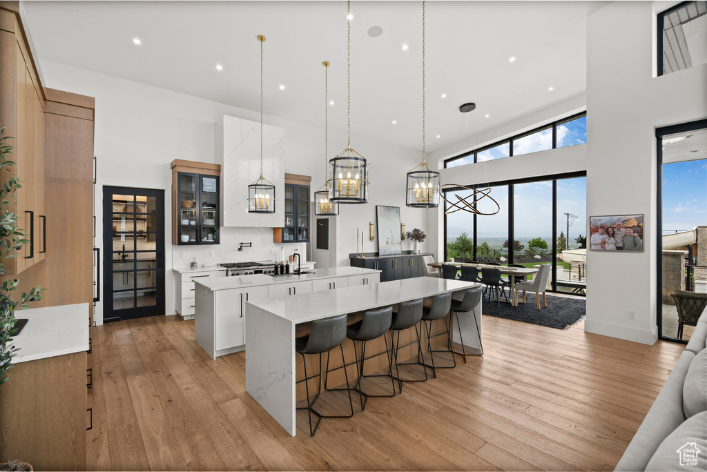 Kitchen with a large island with sink, a high ceiling, light wood-style floors, glass insert cabinets, and a kitchen breakfast bar