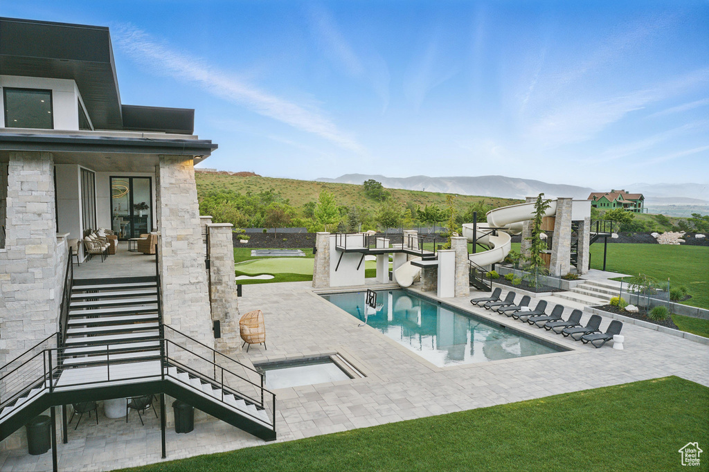 View of swimming pool featuring stairs, a mountain view, a water slide, a patio area, and a yard