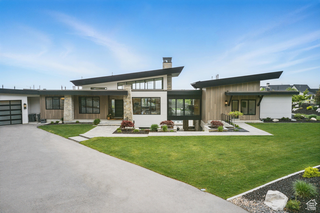 Back of property with a chimney, a lawn, asphalt driveway, and a garage