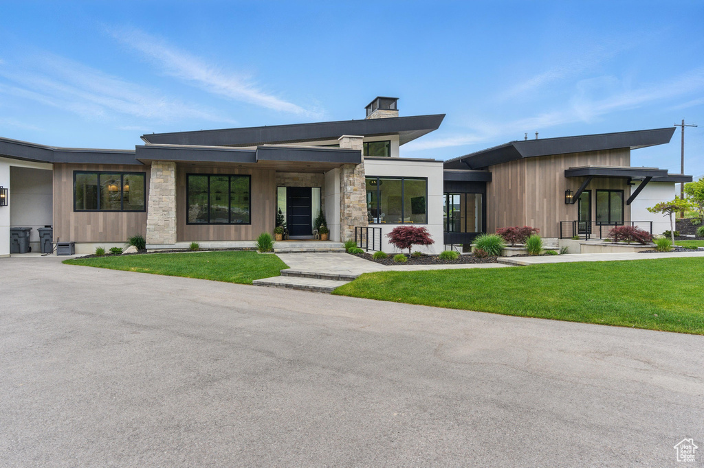 Modern home with a front yard, a chimney, stone siding, and covered porch