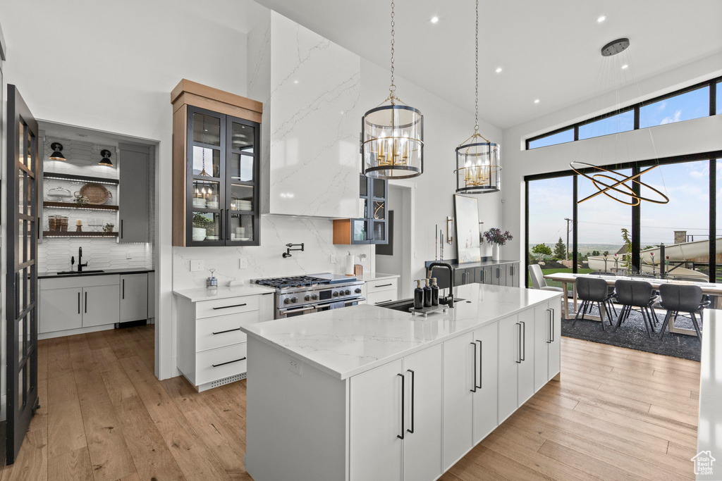 Kitchen with a sink, a high ceiling, high end stainless steel range, an island with sink, and light wood-style flooring