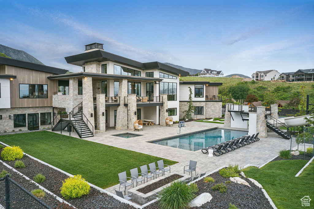 Back of property with a balcony, a lawn, and stone siding