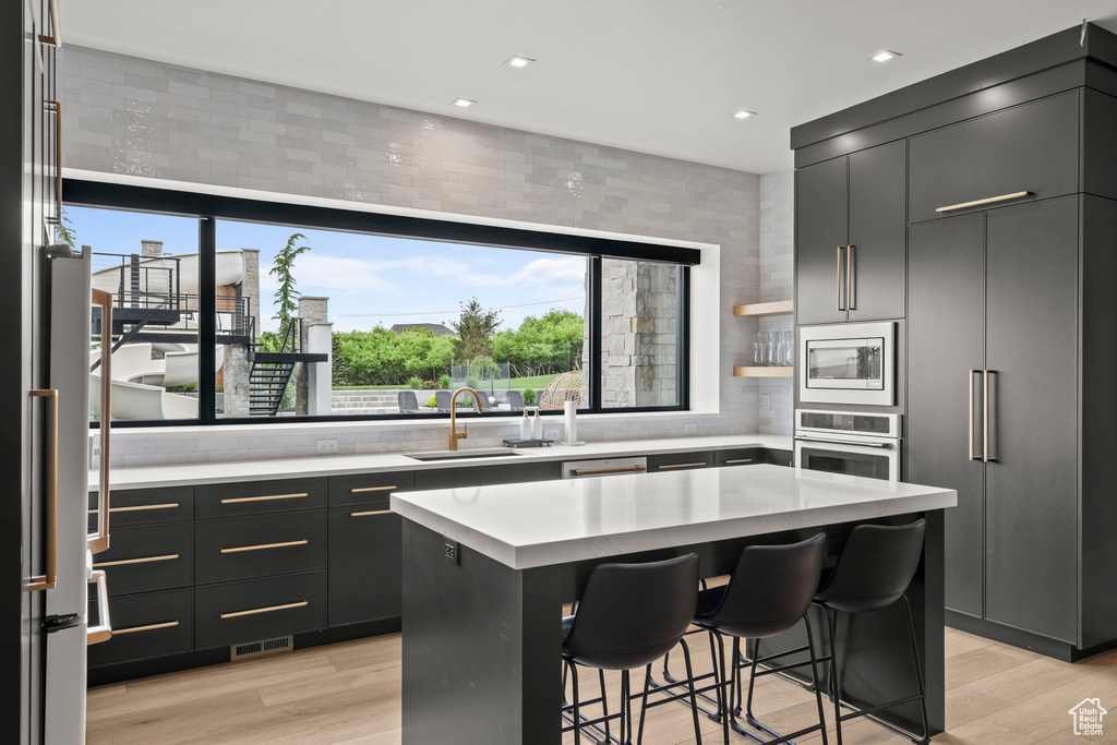 Kitchen with appliances with stainless steel finishes, light countertops, a breakfast bar, a sink, and light wood-style flooring